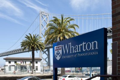 Sign for Wharton University of Pennsylvania in front of palm trees and a large suspension bridge.