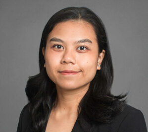 Acacio, Alyzza_final Headshot of a person with long dark hair, wearing a dark blazer, set against a plain gray background.