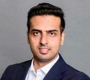 Choudhary, Gaurav Singh_final Headshot of a person with short dark hair, wearing a suit jacket and white collared shirt, set against a neutral background.