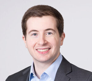 Washington DC, US, February 2023 Headshot of a smiling person in a suit jacket and light blue shirt against a plain background.