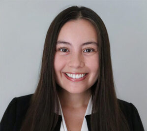 Ho, Kaitlyn_final Headshot of a smiling person with long, straight hair, wearing a black blazer and a white shirt against a neutral background.