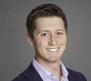 Johnson, Christman Lange (Chris)_final A headshot of a person with short hair, smiling, wearing a suit jacket and a collared shirt against a neutral background.