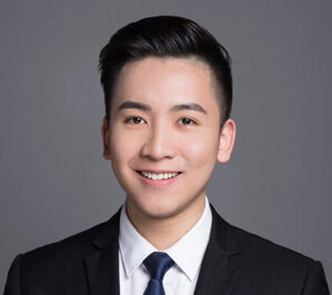 Li, Charles_final Headshot of a person wearing a dark suit, white shirt, and blue tie, set against a plain gray background.