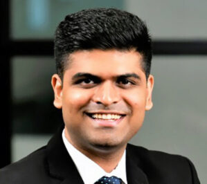 Mittal, Sakansh_final Headshot of a person in a suit and tie, smiling in an indoor setting.