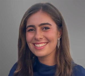Weissman, Lizzie_final Smiling headshot of a person with long brown hair, wearing a blue top and a dangling earring.