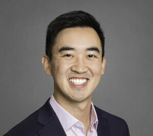 Yuan, Edward Bryan_final This is a headshot of a smiling person wearing a dark blazer and light-colored shirt against a plain background.